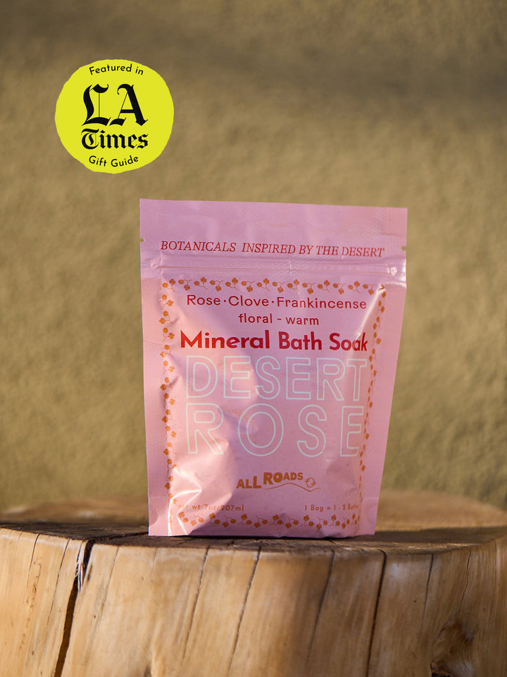 Pink package of Desert Rose Mineral Bath Soak on a wooden surface with a blurred natural background.