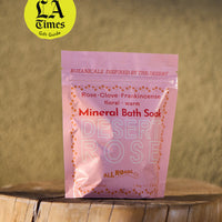Pink package of Desert Rose Mineral Bath Soak on a wooden surface with a blurred natural background.