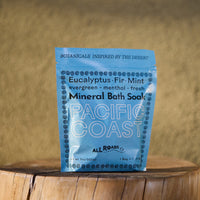 Blue package of Pacific Coast Mineral Bath Soap on a wooden surface with a blurred natural background