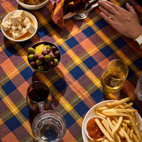 A plaid tablecloth with pink and blue squares is laid out on a table, covering a meal including fries, grapes, bread, and drinks.