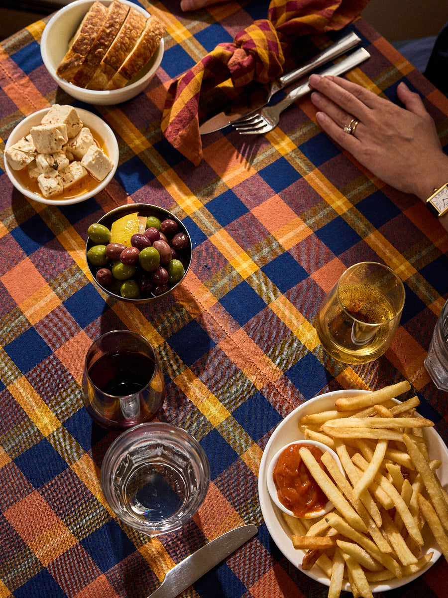 A plaid tablecloth with pink and blue squares is laid out on a table, covering a meal including fries, grapes, bread, and drinks.