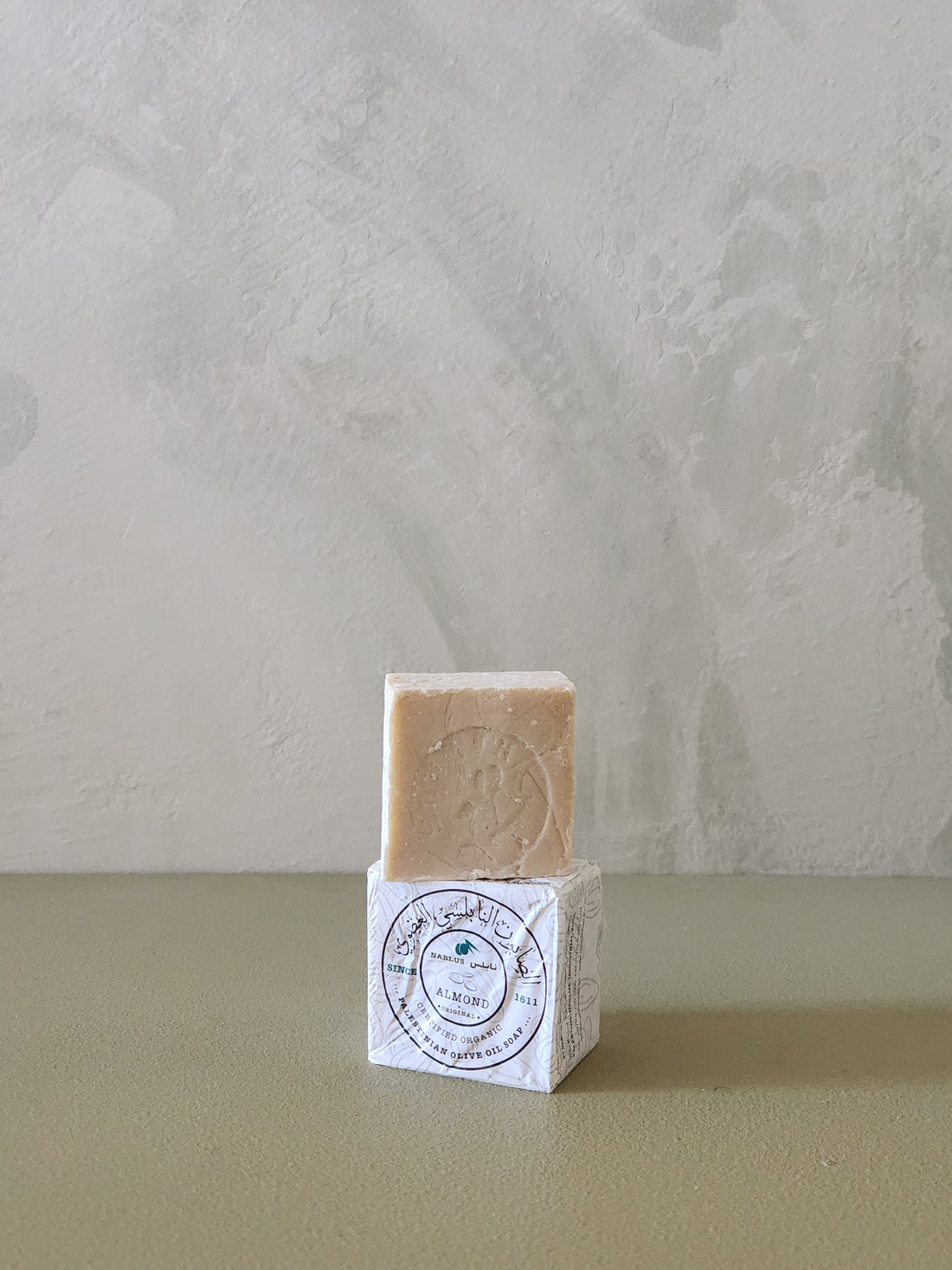 Bar of soap on a white cube with a label against a textured light gray background