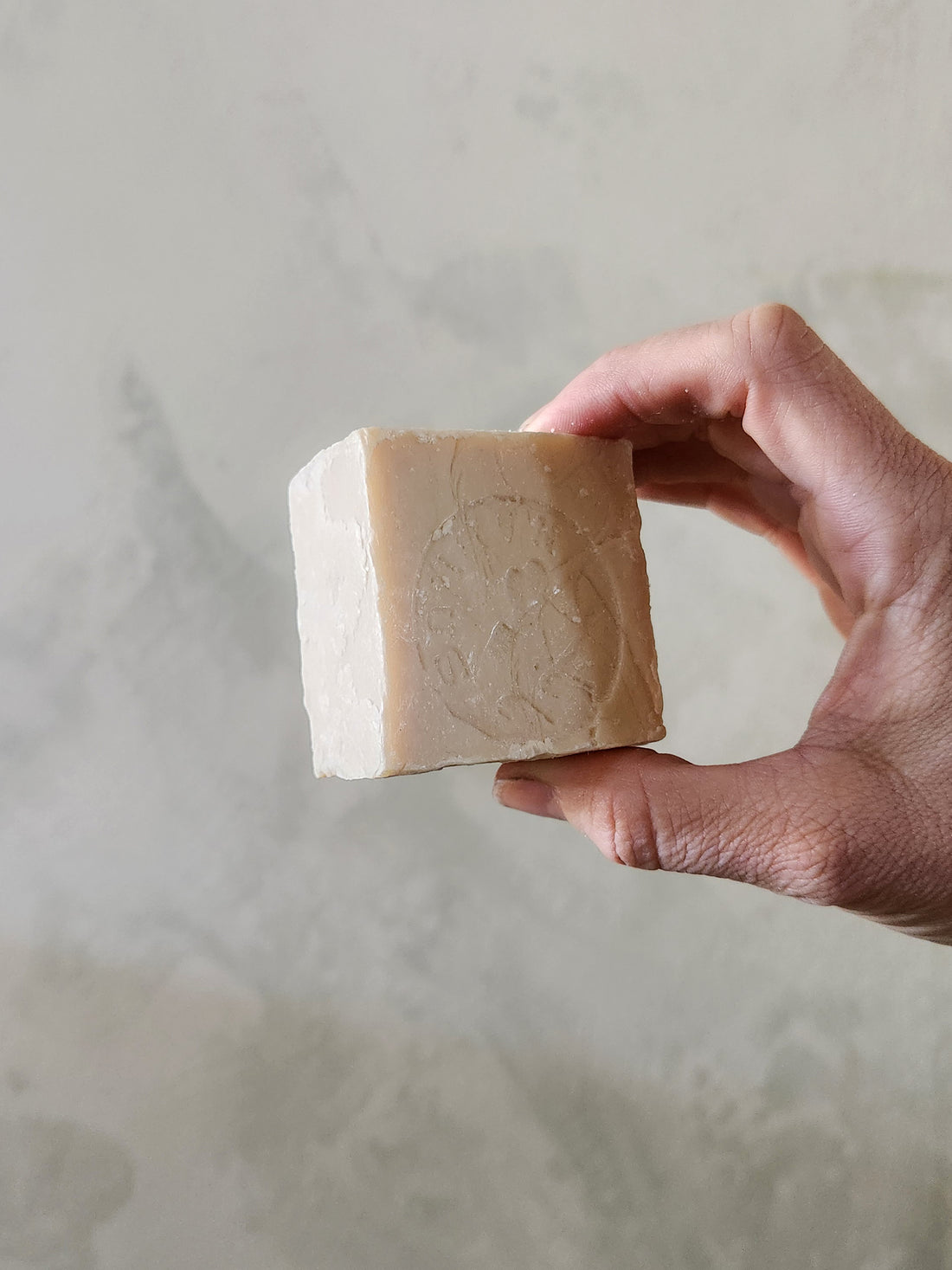 Hand holding a bar of soap against a neutral background
