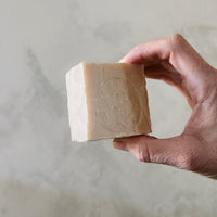 Hand holding a bar of soap against a neutral background
