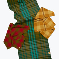 Three plaid tablelinens in different colorways (green/teal, mustard yellow, and red) arranged on a light gray background.