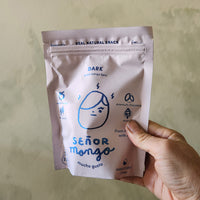 Hand holding a white snack package with blue text and branding against a plain background