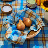 Two pears in a wooden bowl on a checkered tablecloth with a plate of toast and a vase of sunflowers.
