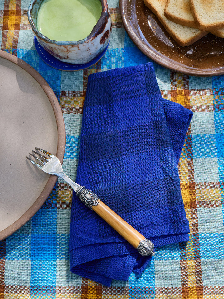 Blue checkered napkin on a plaid tablecloth with a plate, fork, and bowl.