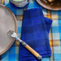 Blue checkered napkin on a plaid tablecloth with a plate, fork, and bowl.