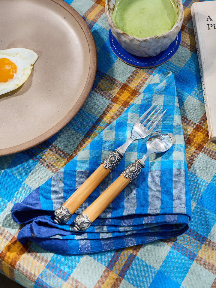 Table setting with a plate, egg, cup of green tea, and decorative cutlery on a checkered tablecloth.