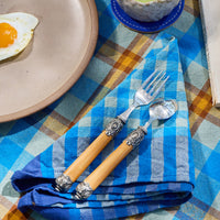 Table setting with a plate, egg, cup of green tea, and decorative cutlery on a checkered tablecloth.