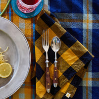 Table setting with a plaid tablecloth, silverware, and a glass of red wine.