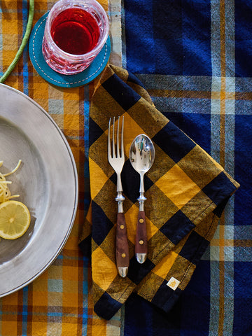 Table setting with a plaid tablecloth, silverware, and a glass of red wine.