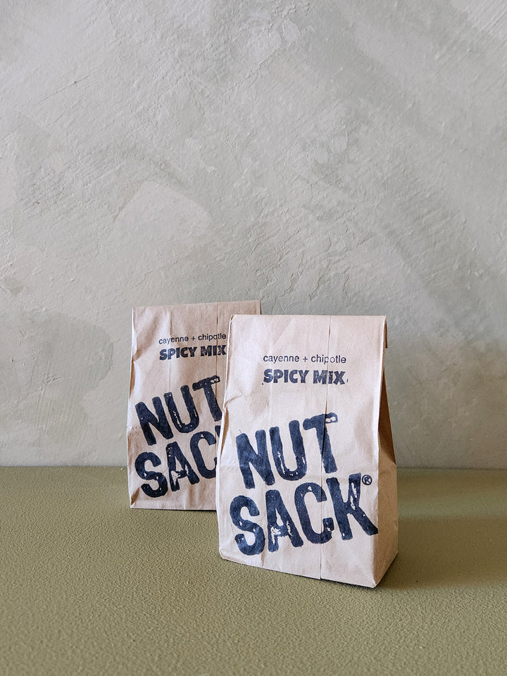 Two 'Nut Sack' spicy mix packages on a textured surface with a neutral background