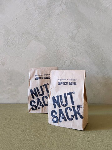 Two 'Nut Sack' spicy mix packages on a textured surface with a neutral background