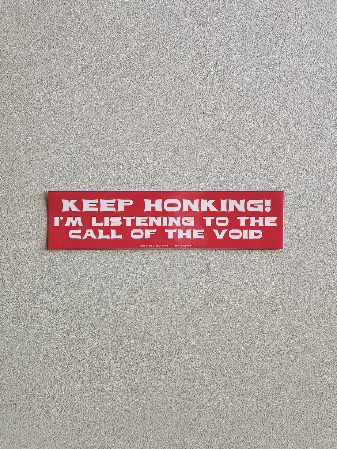 Red bumper sticker with text on a gray background