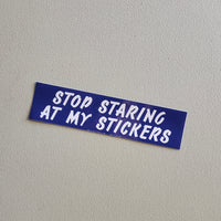 Blue sticker with white text 'STOP STARING AT MY STICKERS' on a gray background