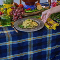Table setting with pasta dish, fruit, and a candle on a blue plaid tablecloth.