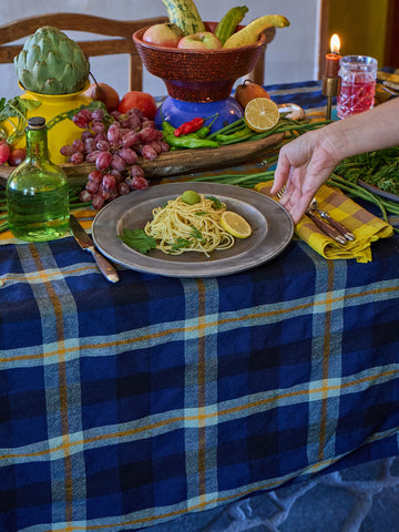 Table setting with pasta dish, fruit, and a candle on a blue plaid tablecloth.