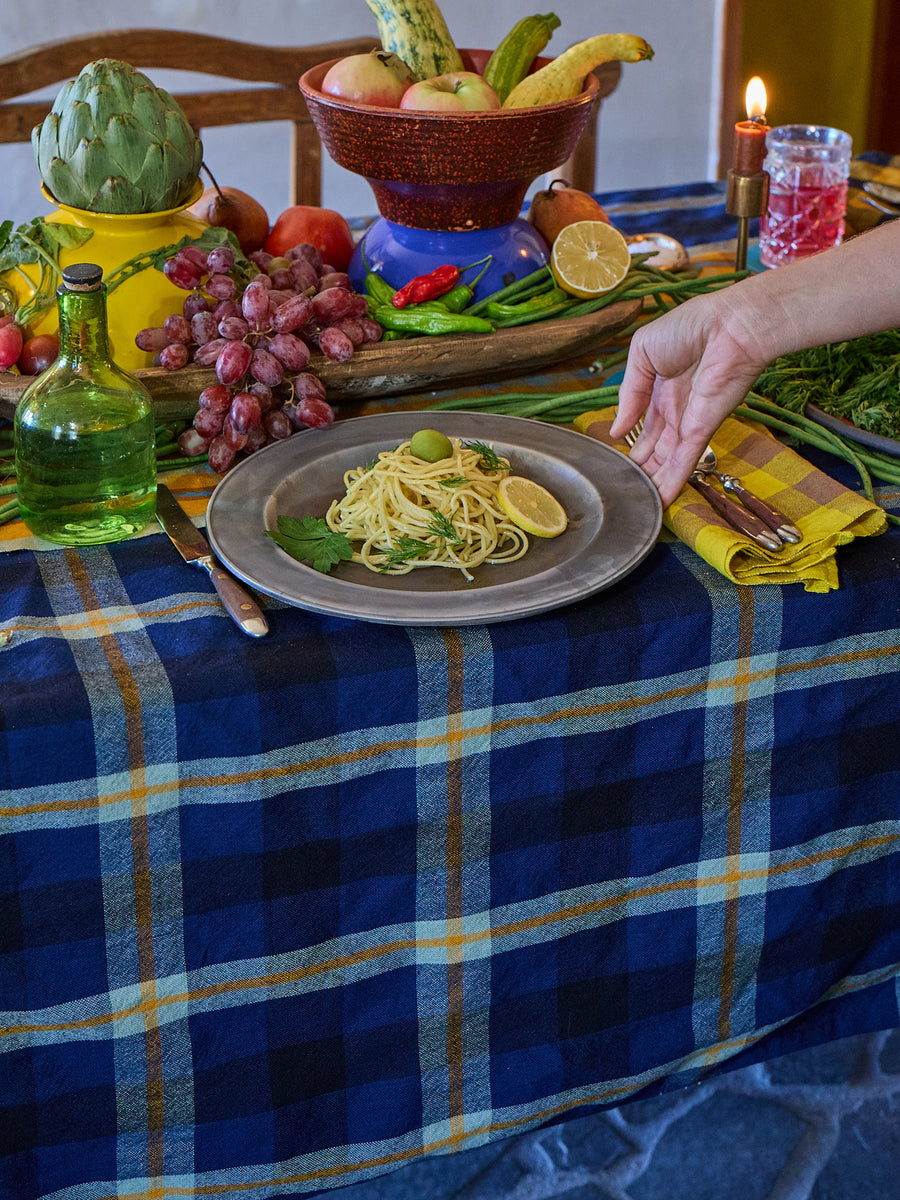 Table setting with pasta dish, fruit, and a candle on a blue plaid tablecloth.