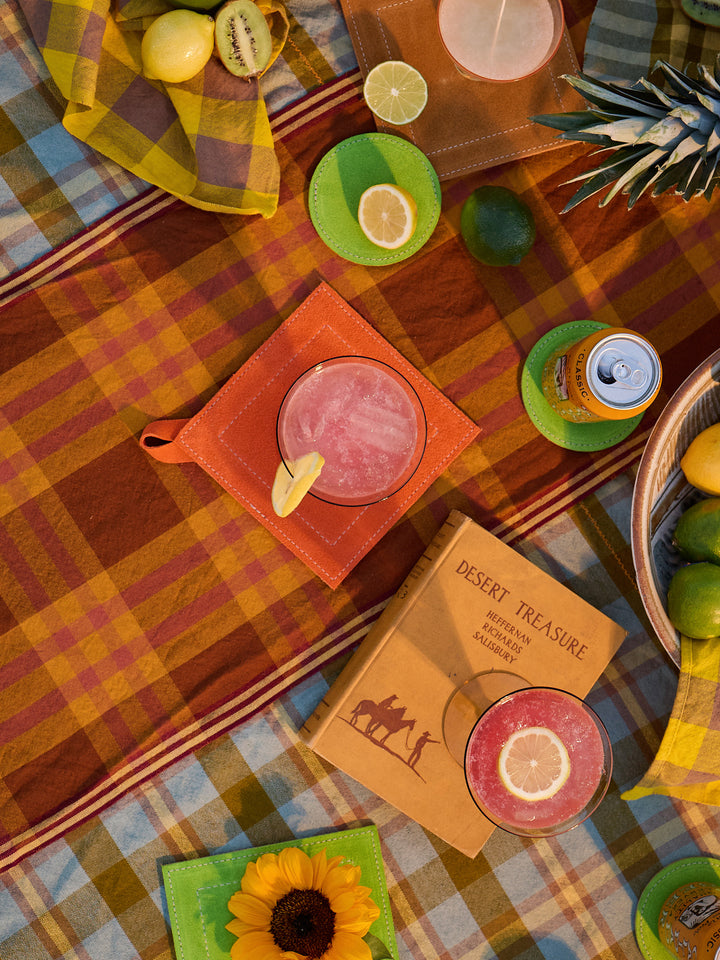 Colorful picnic setup with drinks, snacks, and a book on a checkered blanket.