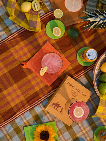 Colorful picnic setup with drinks, snacks, and a book on a checkered blanket.