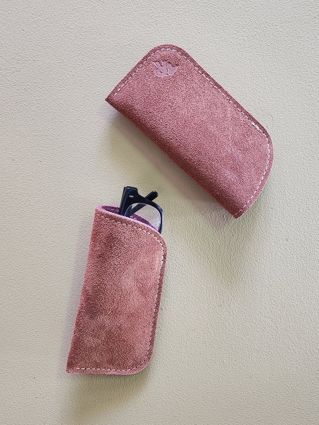 Rust suede eyeglass case with a smaller rust case containing glasses on a light gray background