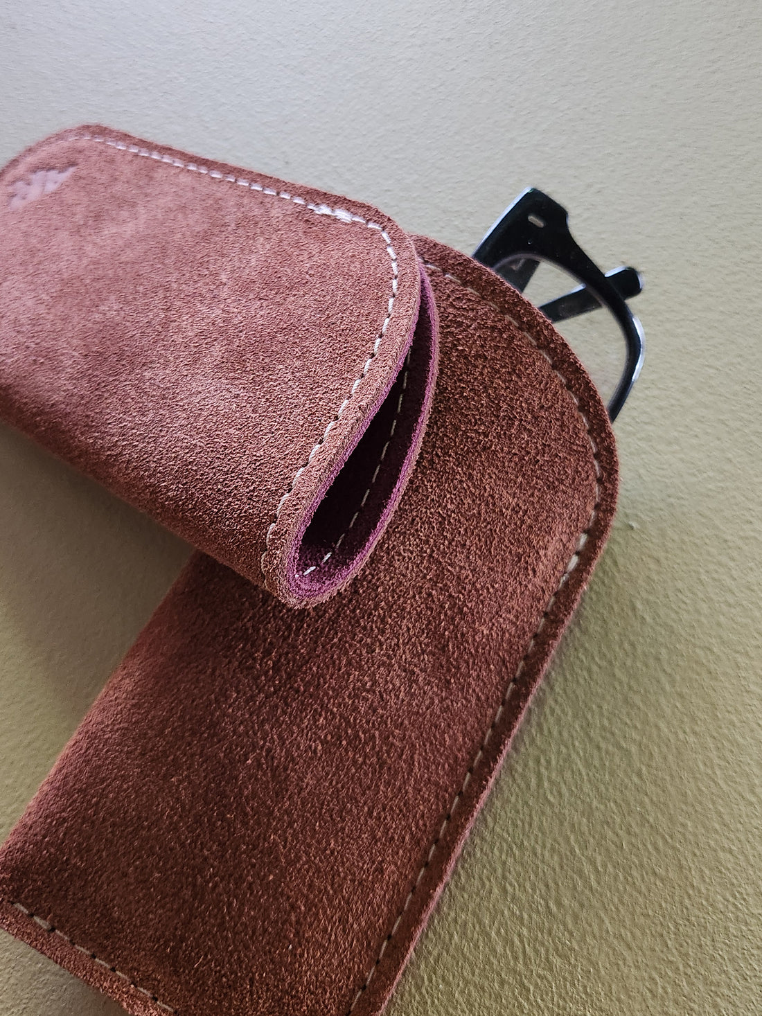 Brown suede pouch with a purple interior on a beige surface