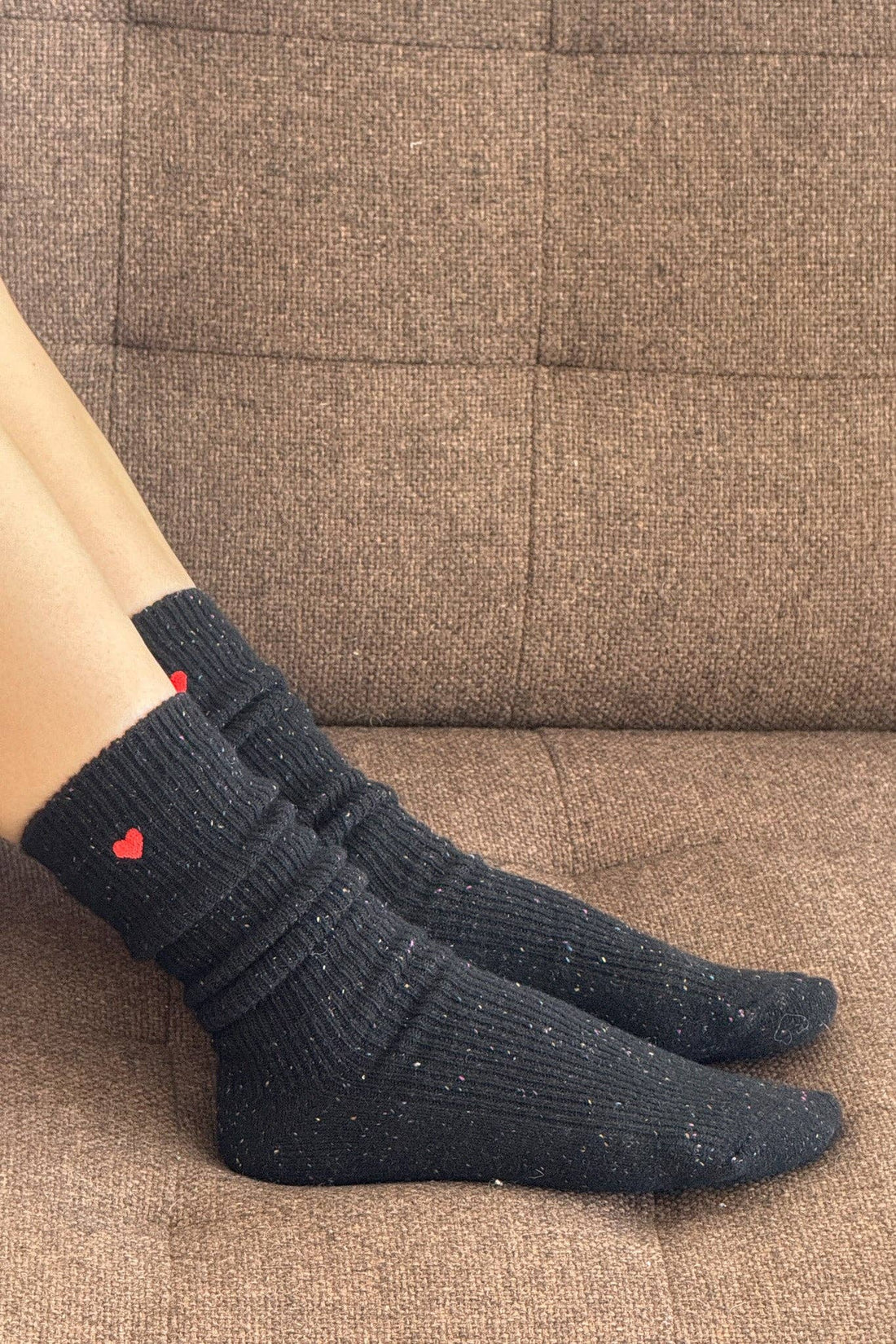Person wearing black socks with red hearts on a brown couch.