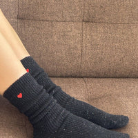 Person wearing black socks with red hearts on a brown couch.