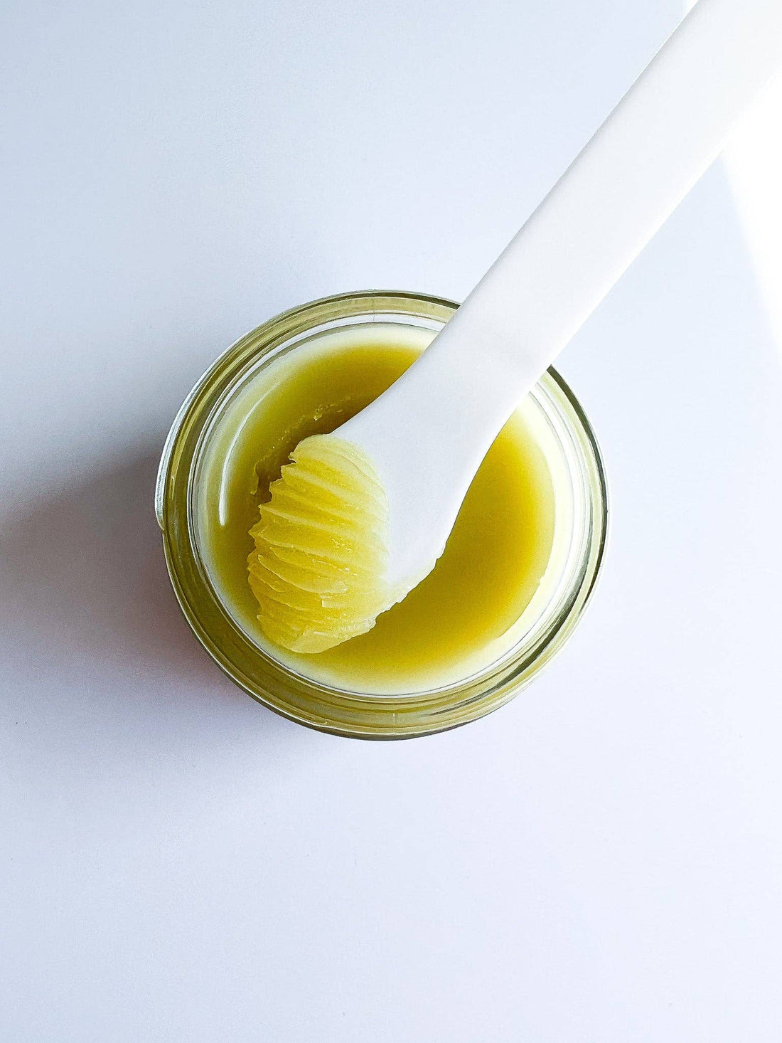 Jar of yellow cream with a white applicator on a light gray background