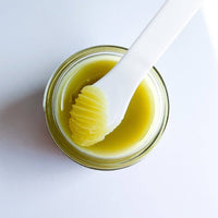 Jar of yellow cream with a white applicator on a light gray background