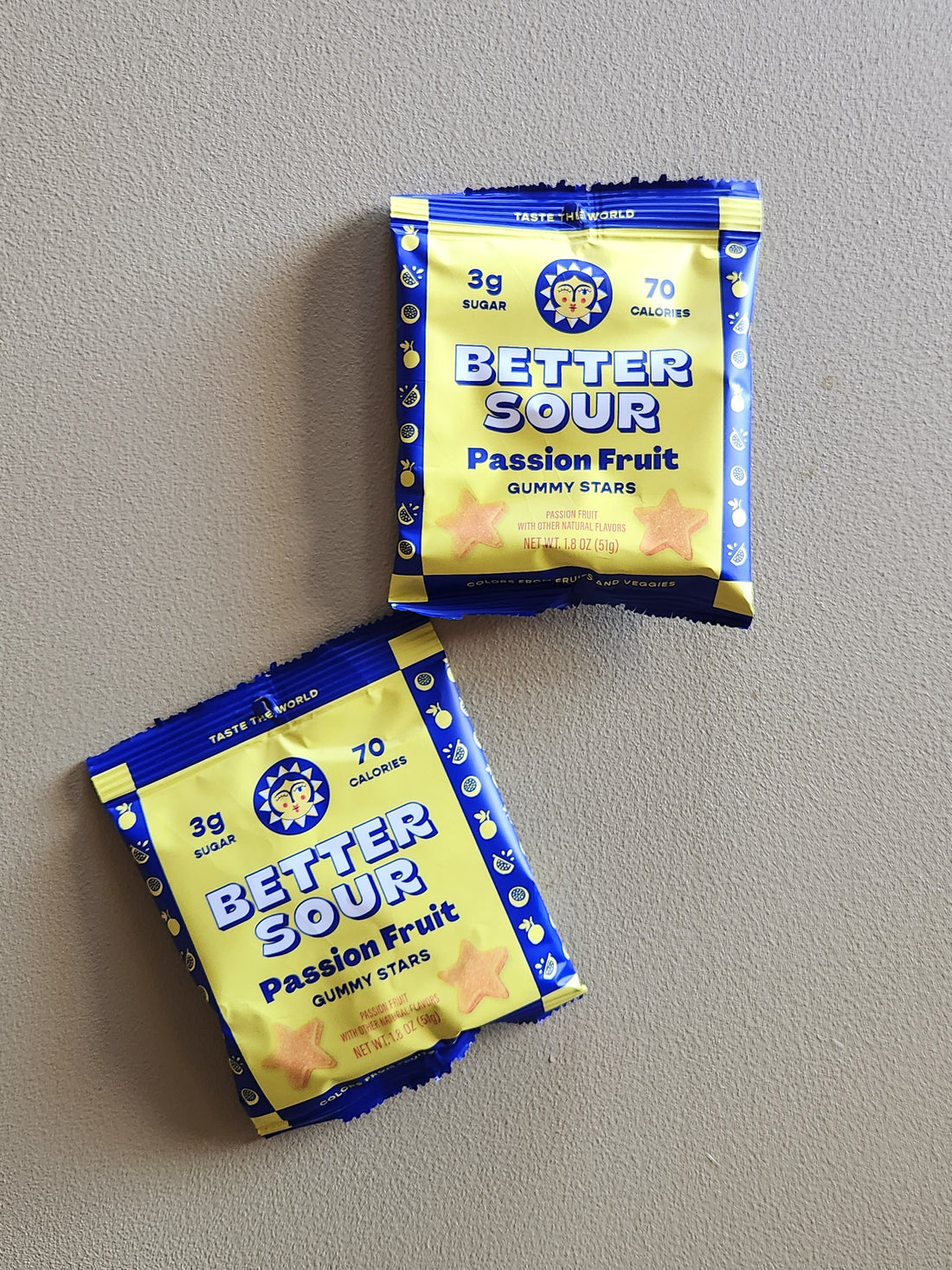 Two packs of Better Sour Passion Fruit Gummy Stars candy arranged on a neutral gray background.