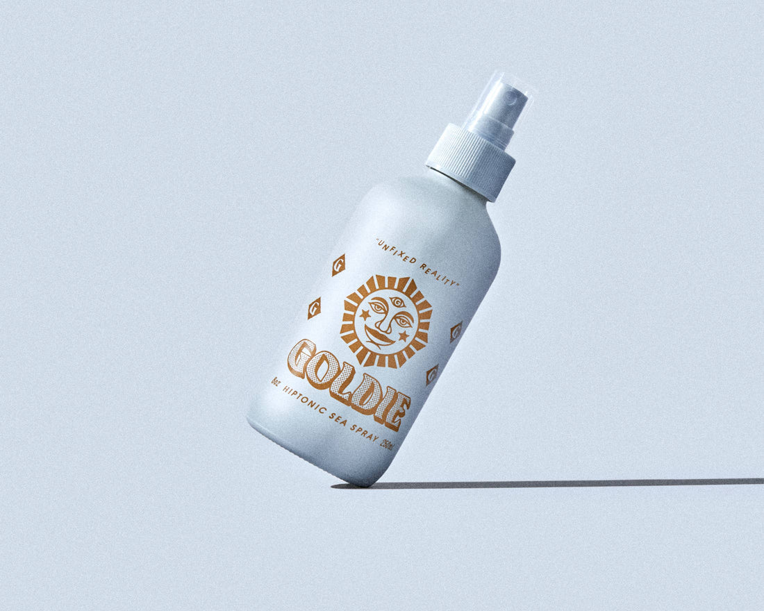White spray bottle with gold text on a light blue background