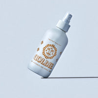 White spray bottle with gold text on a light blue background