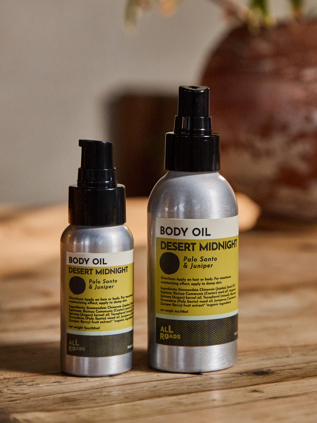 Two silver spray bottles of Body Oil by All Roads, one smaller and one larger, labeled &