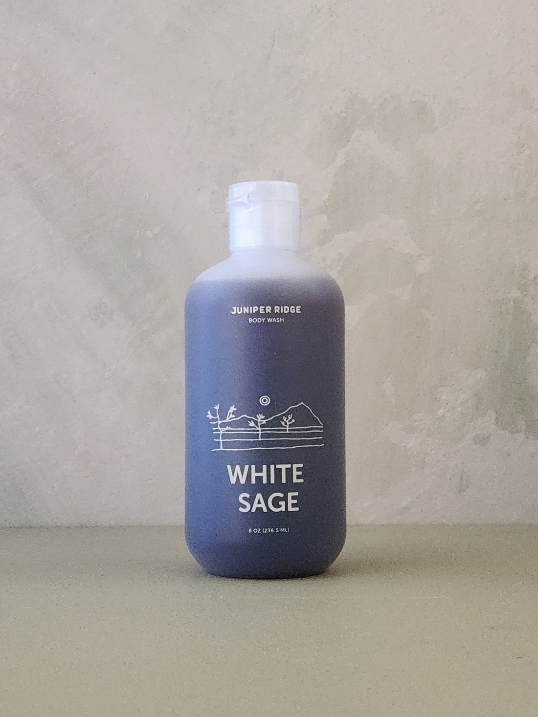Blue bottle of Juniper Ridge White Sage body wash on a textured surface with a neutral background
