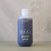 Blue bottle of Juniper Ridge White Sage body wash on a textured surface with a neutral background