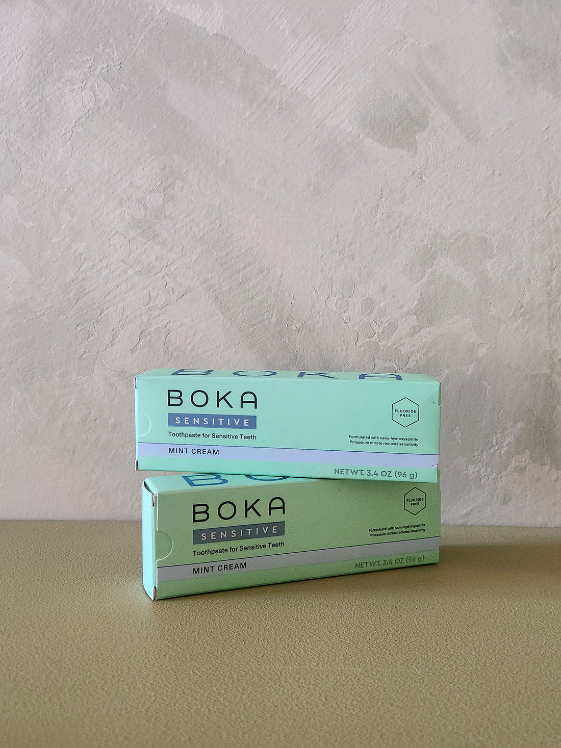 Two boxes of Boka Sensitive Mint Cream toothpaste stacked on a beige surface against a textured light gray wall.