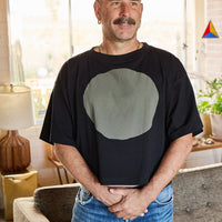 Man wearing a black t-shirt with a grey circle design in a living room setting