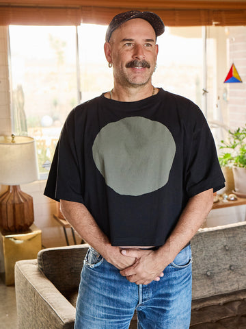 Man wearing a black t-shirt with a grey circle design in a living room setting
