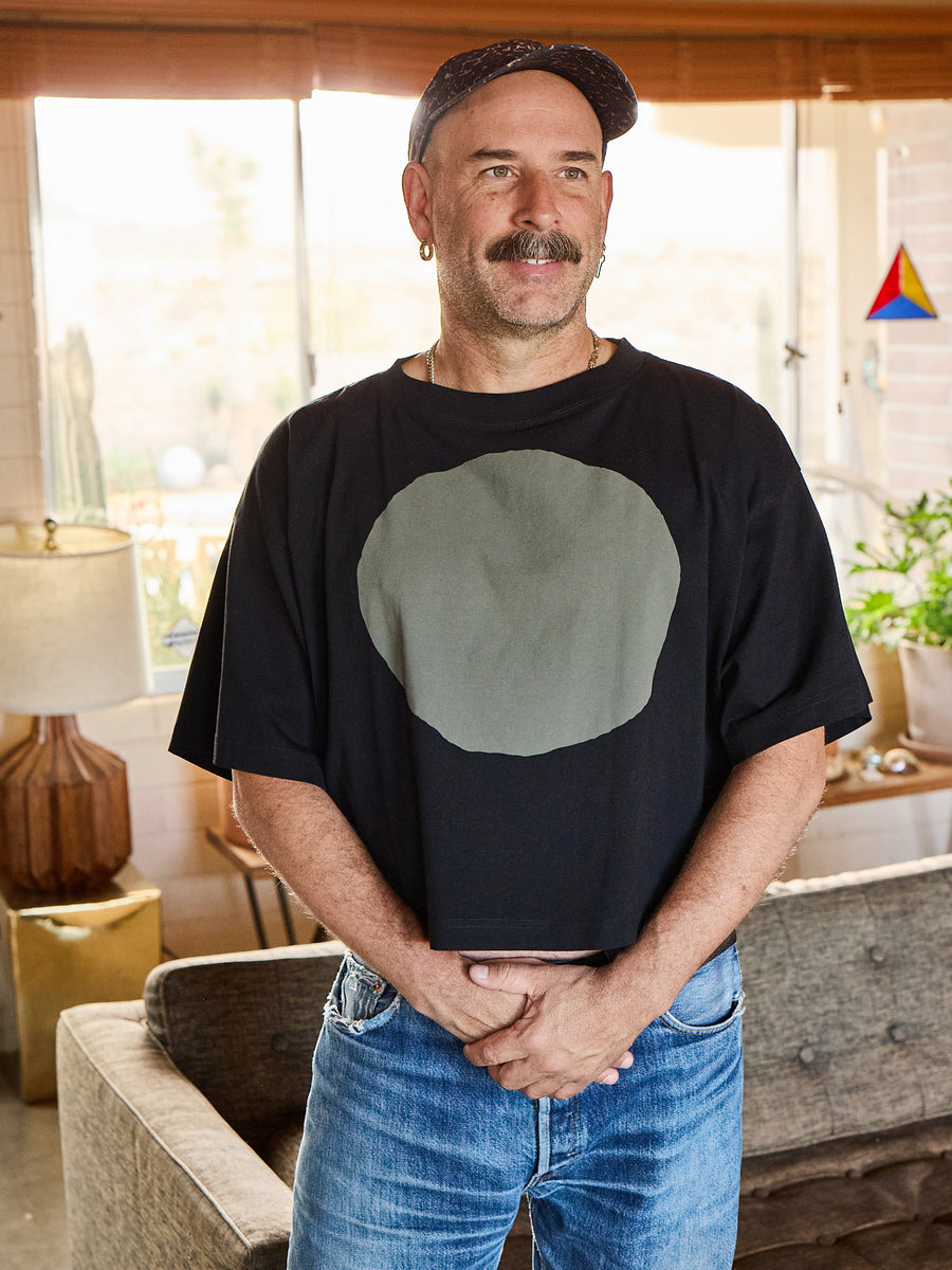 Man wearing a black t-shirt with a grey circle design in a living room setting