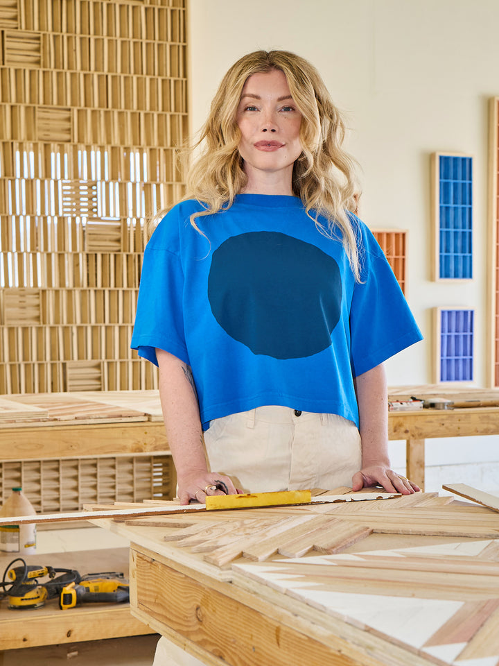 Woman in a blue shirt standing in a workshop with wooden elements.