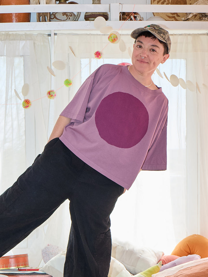 Person wearing a purple t-shirt with a large round design, standing in a room with decorative elements.