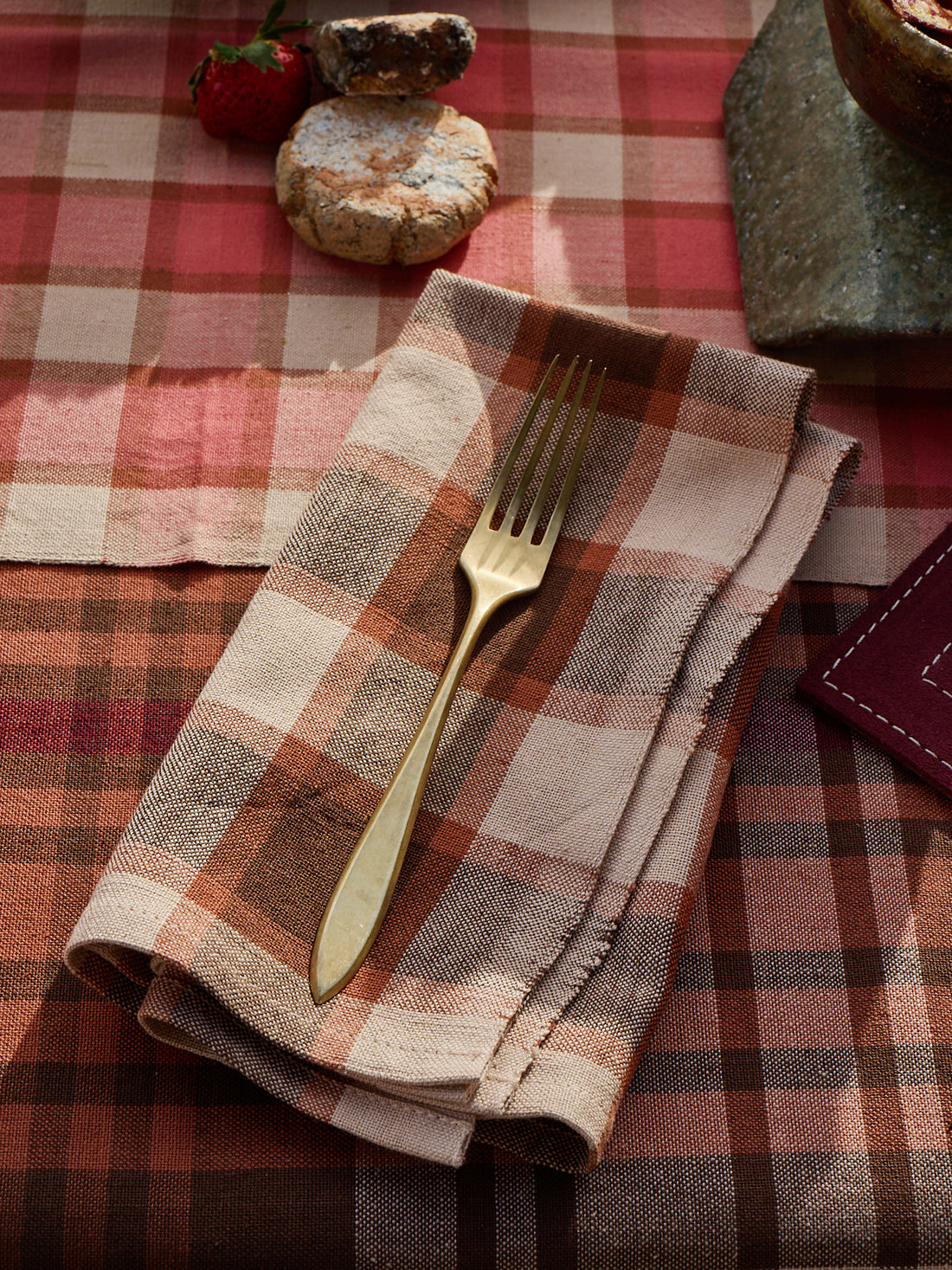Folded plaid napkin with a gold fork on a red and brown checkered tablecloth.