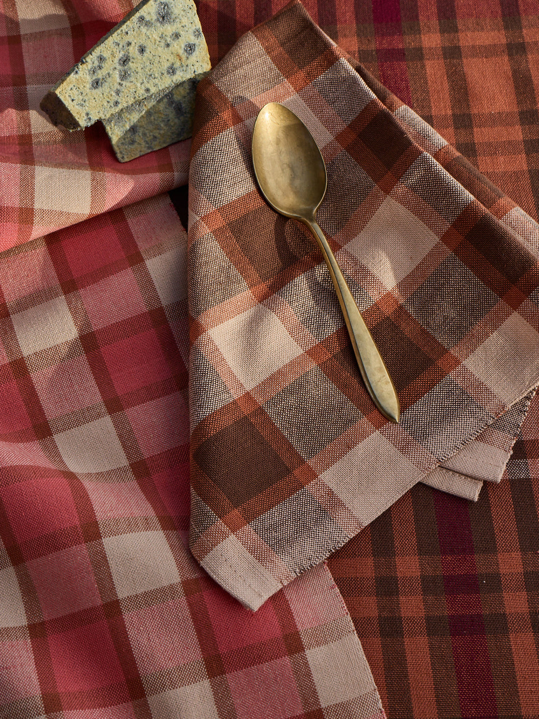 Gold spoon on a plaid fabric with a stone and folded fabric in the background