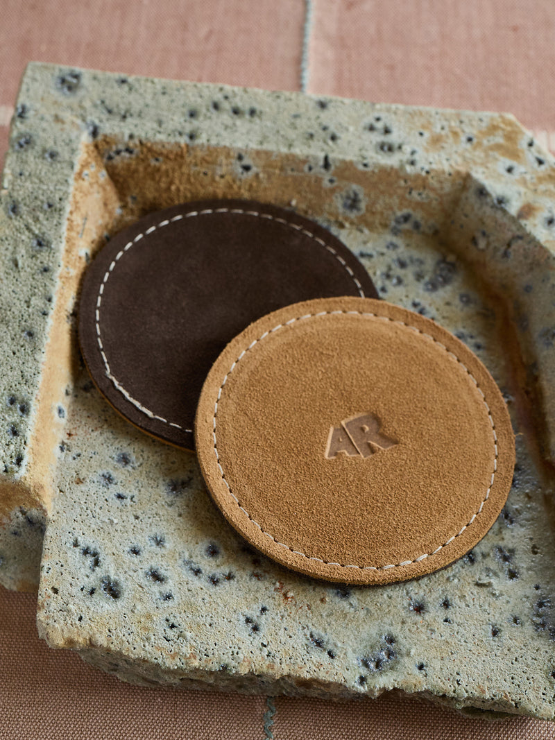 Two leather coasters with a visible brand logo on a textured surface