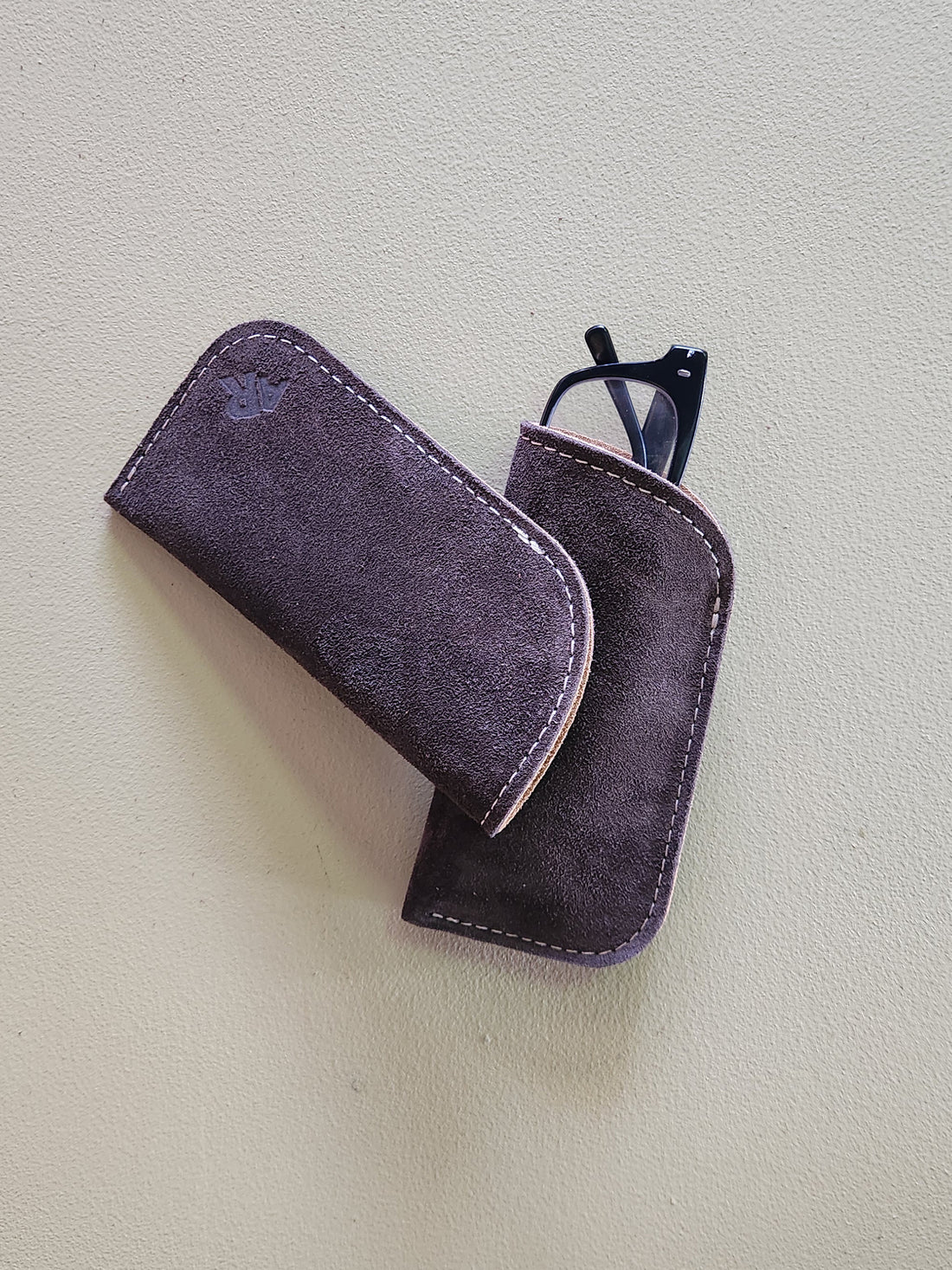 Brown suede glasses case with a pair of glasses on a light gray background