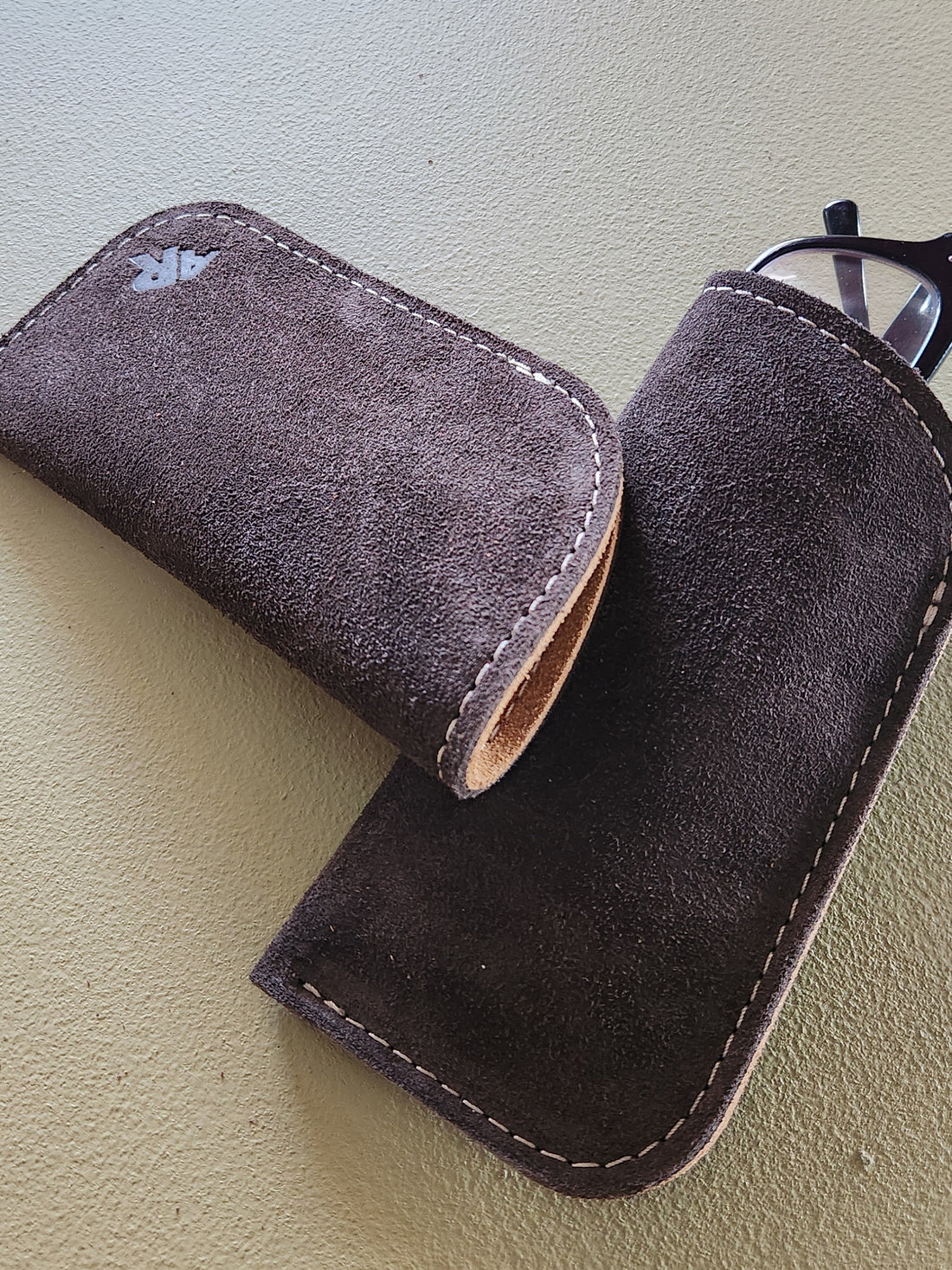 Brown suede glasses case on a light green surface