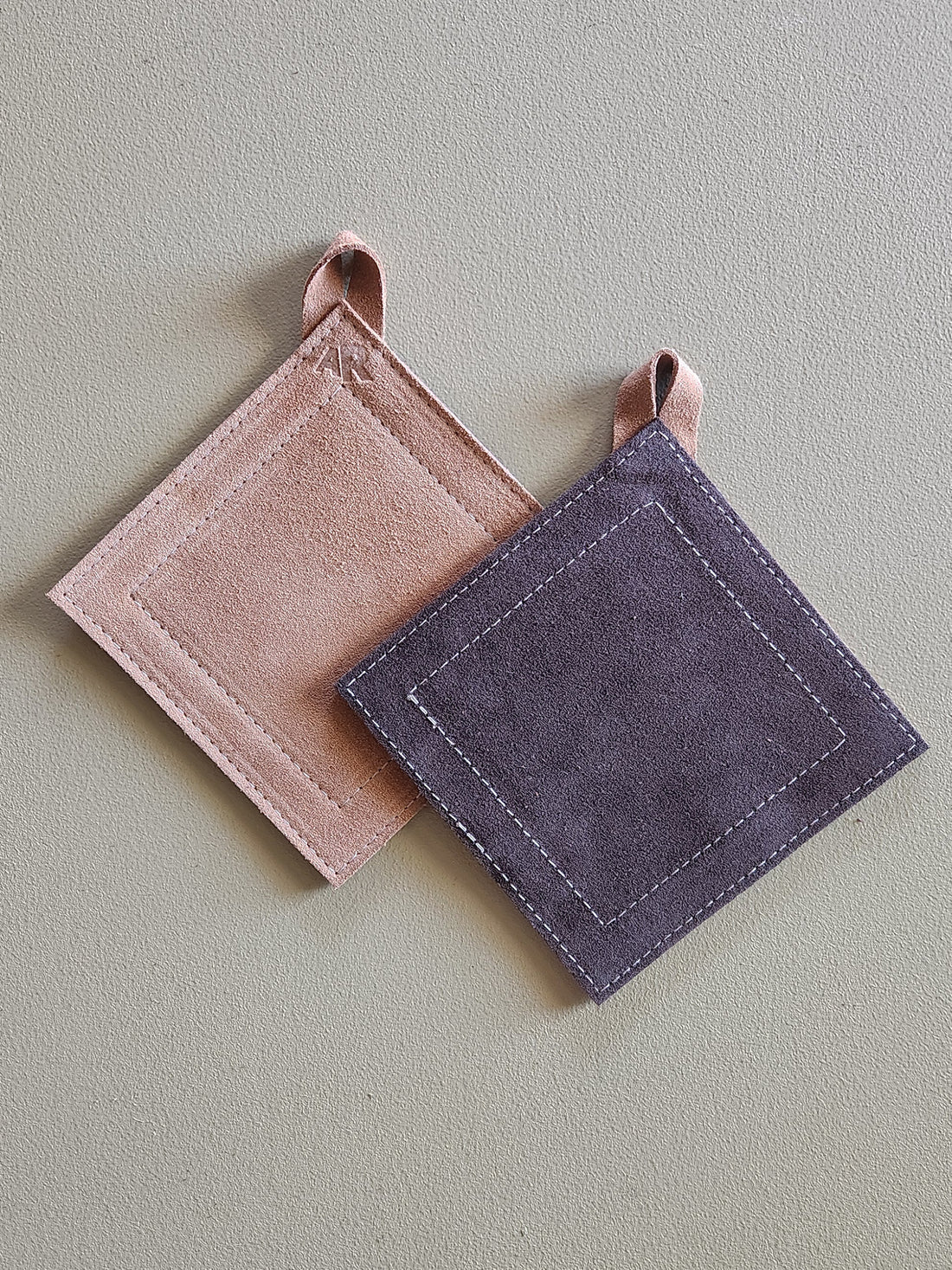 Two square potholders, one tan and one dark brown, on a light gray background.